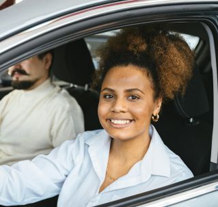 African American woman happily test driving a new car at a dealership. Capturing her joyful expression.